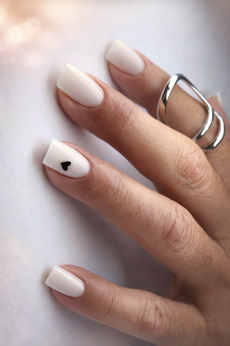 A neutral manicure with a small black heart accent.