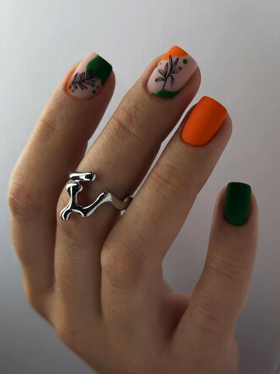 Hand-painted nail art in green and amber tones over a neutral base.
